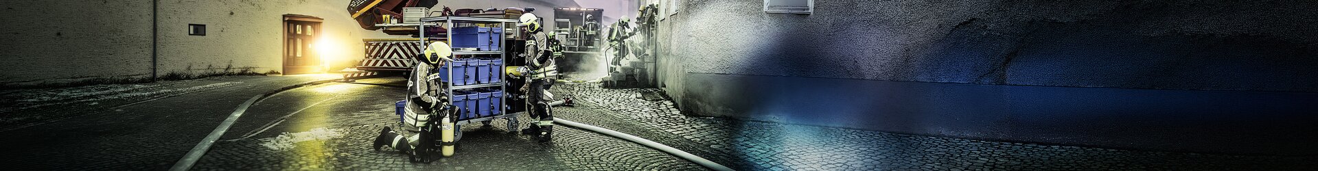 Feuerwehrkräfte arbeiten mit Rollcontainer in schmaler Gasse, Einsatzfahrzeug im Hintergrund | © MUNK GmbH