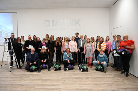 Gruppenfoto der 14 Vertreterinnen und Vertreter der Kindergärten aus Günzburg und Leipheim. Sie stehen in einem Halbkreis zusammen. Die vorderen Personen sitzen auf den Bobbycars und lachen.