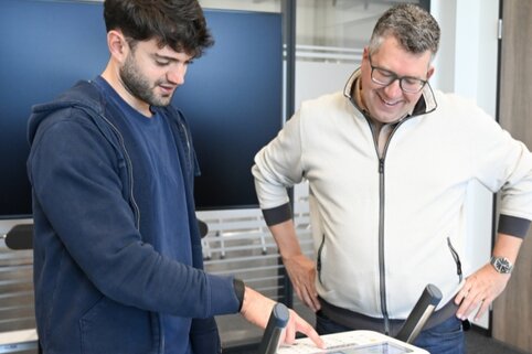 Mitarbeiter misst beim MUNK-Gesundheitstag mit der TK seine Körperwerte an einem Analysegerät, ein Berater der Techniker Krankenkasse erklärt die Ergebnisse.